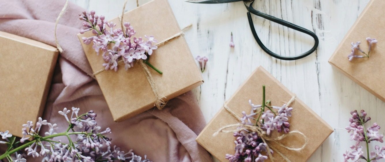 Person wrapping a gift in brown material with a nature theme Person wrapping a gift in brown material with a nature theme in the background, with scissors, string and Christmas decorations around the g